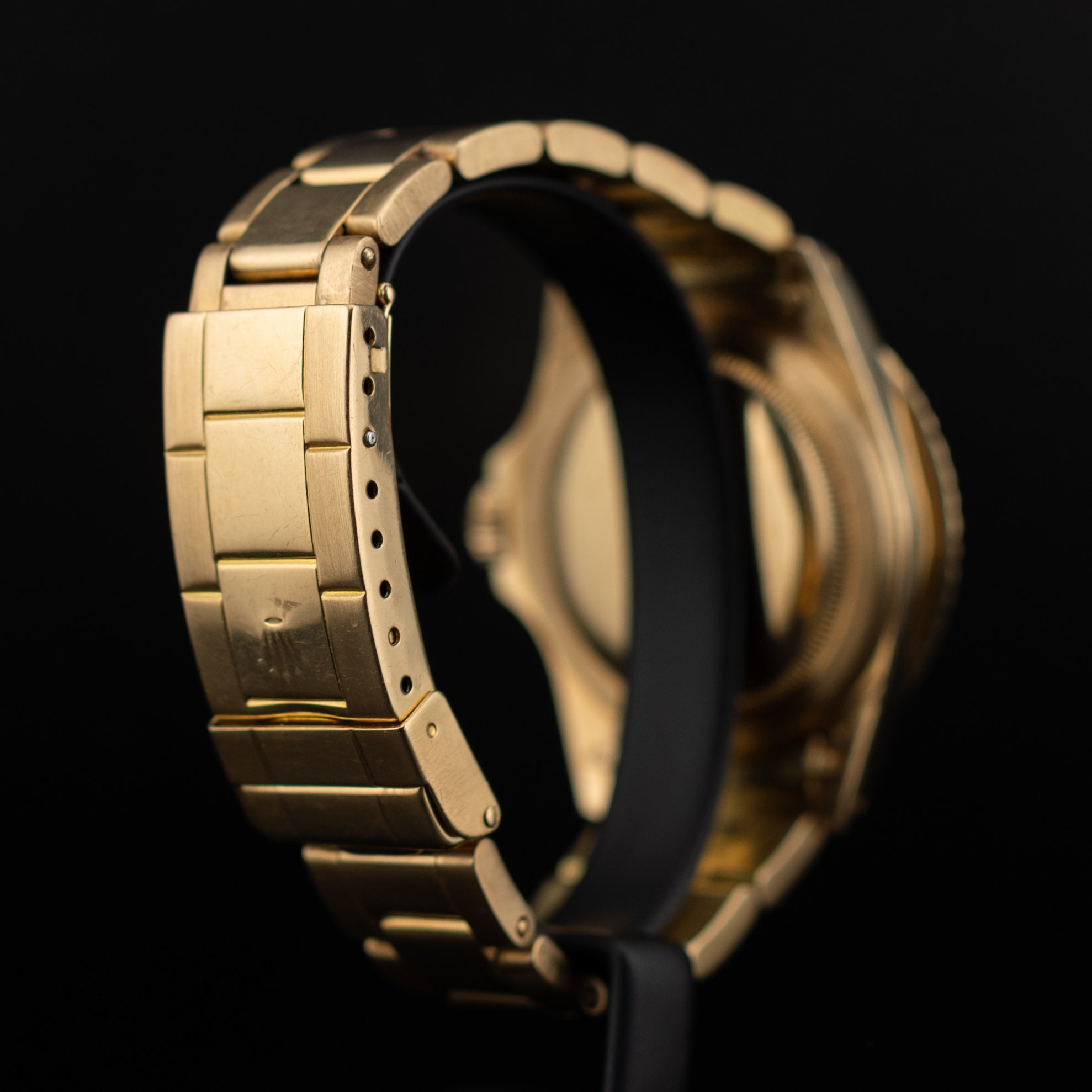 Vue arrière de la Rolex Submariner or jaune sur socle, fond de boîtier visible, bracelet Oyster incurvé et fermoir fermé